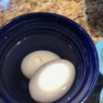 closeup: 2 air fryer soft boiled eggs in a water bath in a small blue bowl