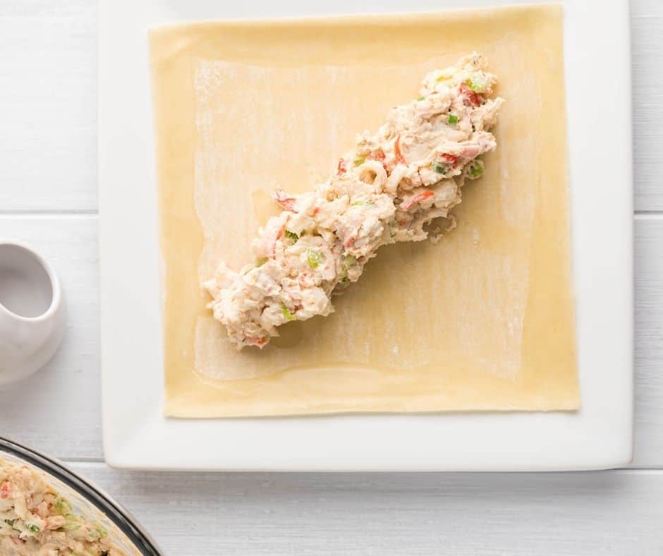 Add 4 tbsp of crab mix diagonally to the center of the egg roll. Fold one corner over the crab mix towards the opposite side, fold both sides over the ends of the crab mix to the center, then tightly roll to the corner.
