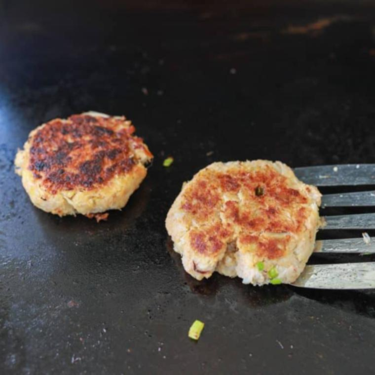 Flipping crab cakes on the Blackstone for even cooking.