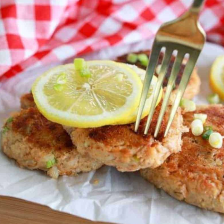 Plate of golden-brown Blackstone crab cakes garnished with fresh herbs and served with a side of dipping sauce.