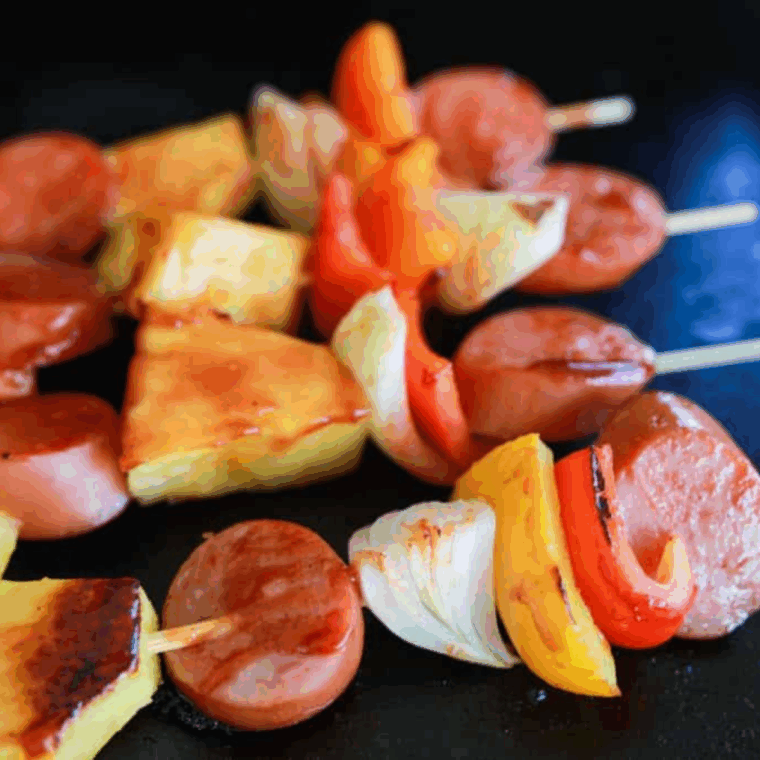 Flipping kabobs on griddle while basting with BBQ sauce for even caramelization.