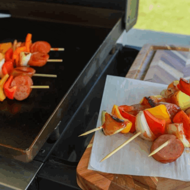 Hawaiian kielbasa kabobs with pineapple and bell peppers cooking on a Blackstone griddle.