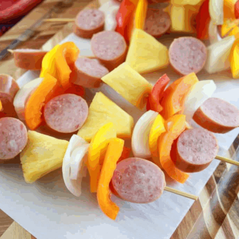 Skewers loaded with kielbasa, bell peppers, onions, and pineapple on a preheated griddle.