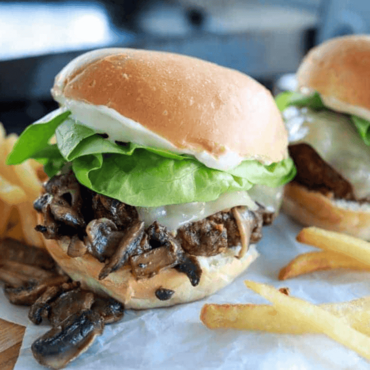 Delicious Blackstone Mushroom Swiss Smash Burgers with sautéed mushrooms, melted Swiss cheese, and crispy beef patties cooked on a griddle.