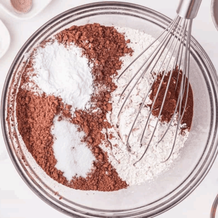 Mixing chocolate cake batter with dry and wet ingredients in bowls, ready for baking in greased cake pans.