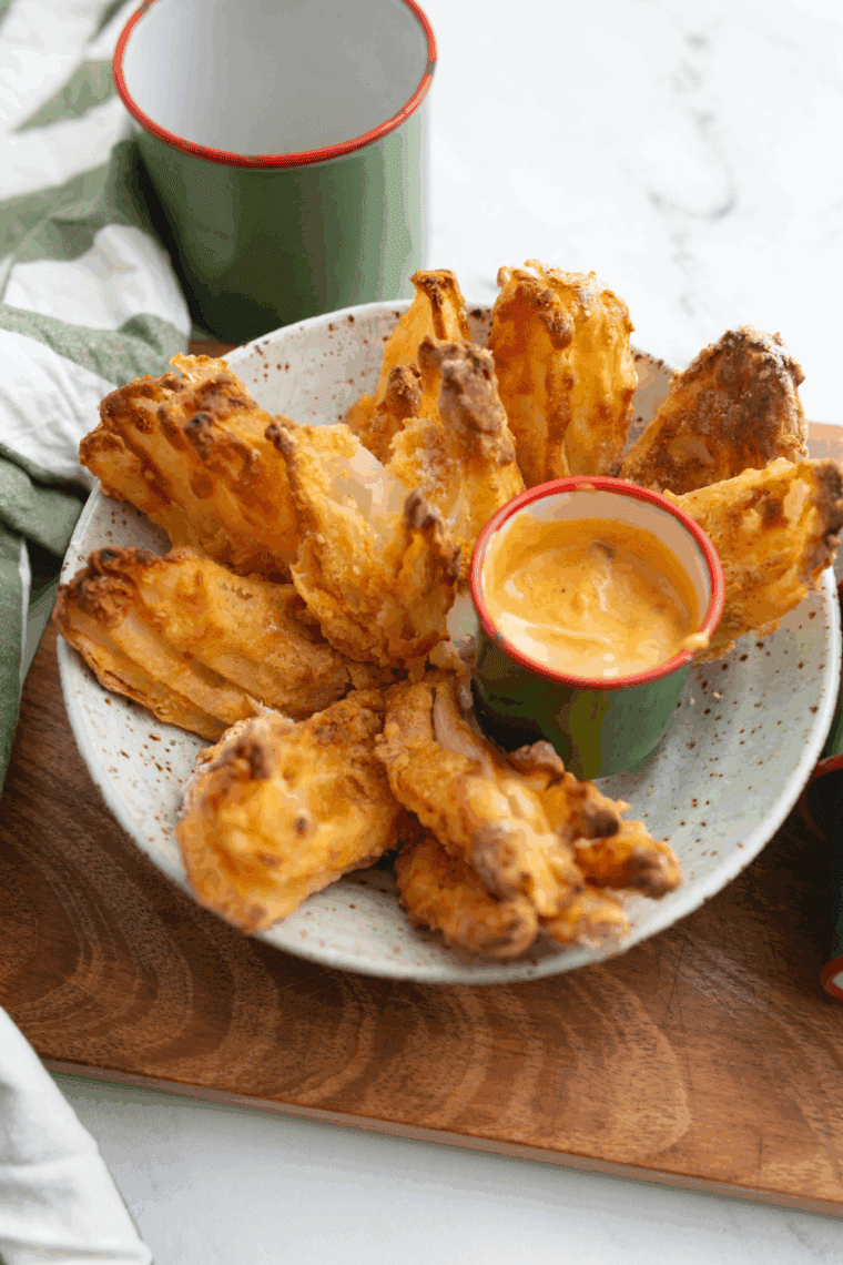 Golden fried Texas Roadhouse-style cactus blossom with dipping sauce on a serving plate.