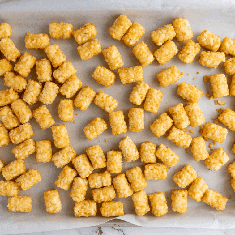 Golden crispy tater tots baking in an oven tray.