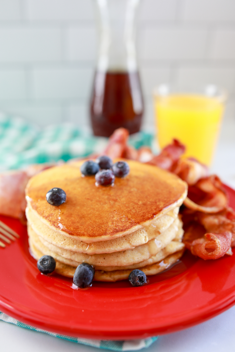 Stack of fluffy Blackstone griddle pancakes golden brown with butter melting and syrup pouring over the top fresh off the griddle.