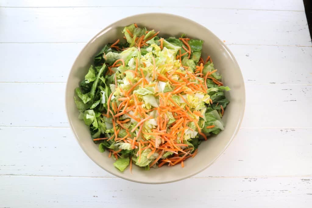 How To Make The Applebee’s Oriental Chicken Salad: While the chicken is cooking, make the salad in a large salad bowl mix together the lettuce, cabbage, shredded carrots, green onions, crispy noodles, and sliced almonds. 