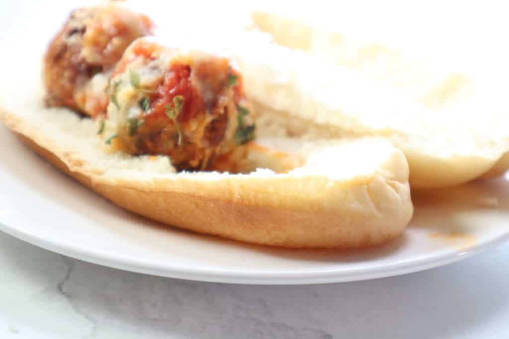 Chicken Parmesan Meatballs placed on a hoagie on a plate. 