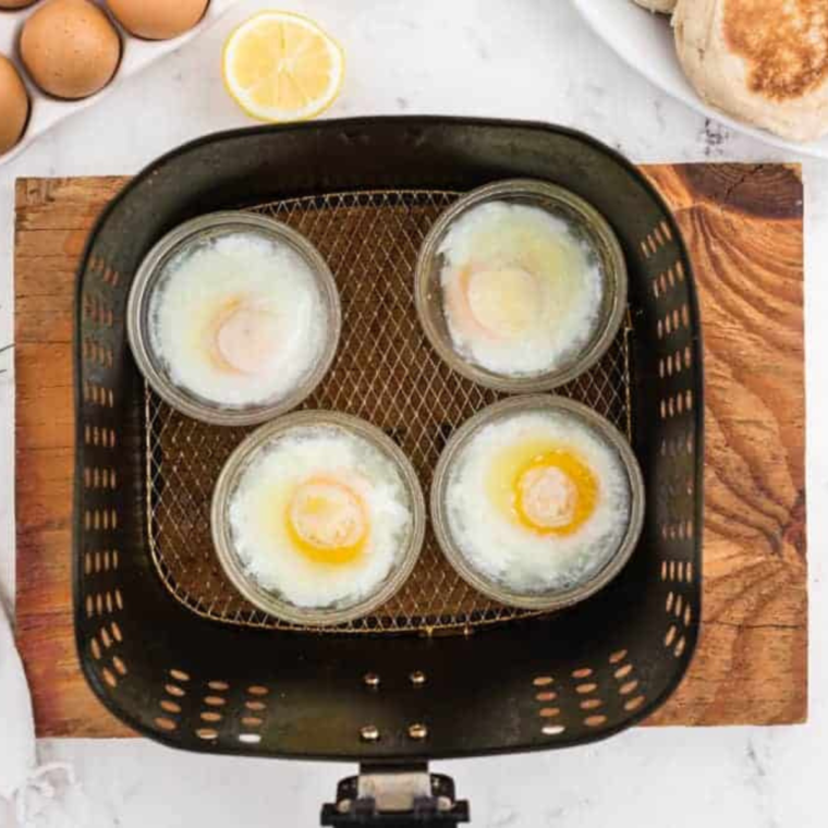 overhead: four ramekins in an air fryer basket with poached eggs in each one