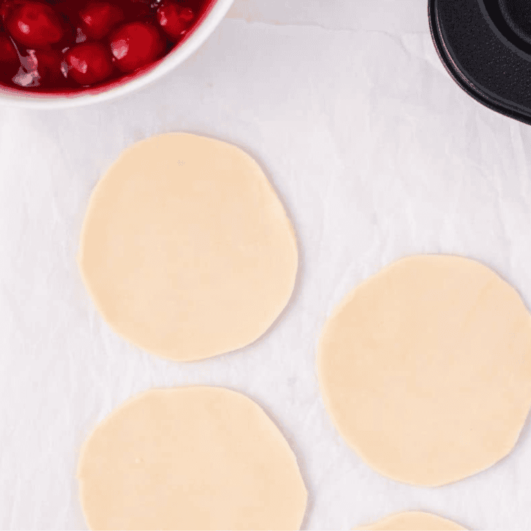 Cutting out pie crust circles to fit inside a muffin tin for Air Fryer Cherry Tarts.