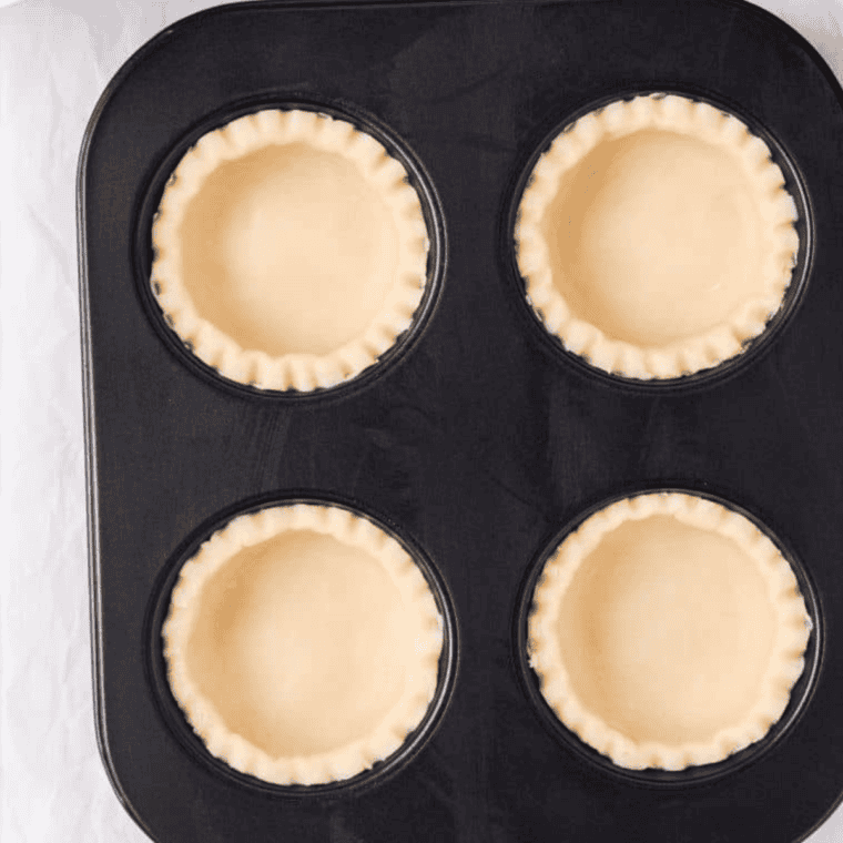 Pie crust dough placed and pressed into a greased muffin tin for Air Fryer Cherry Tarts preparation."