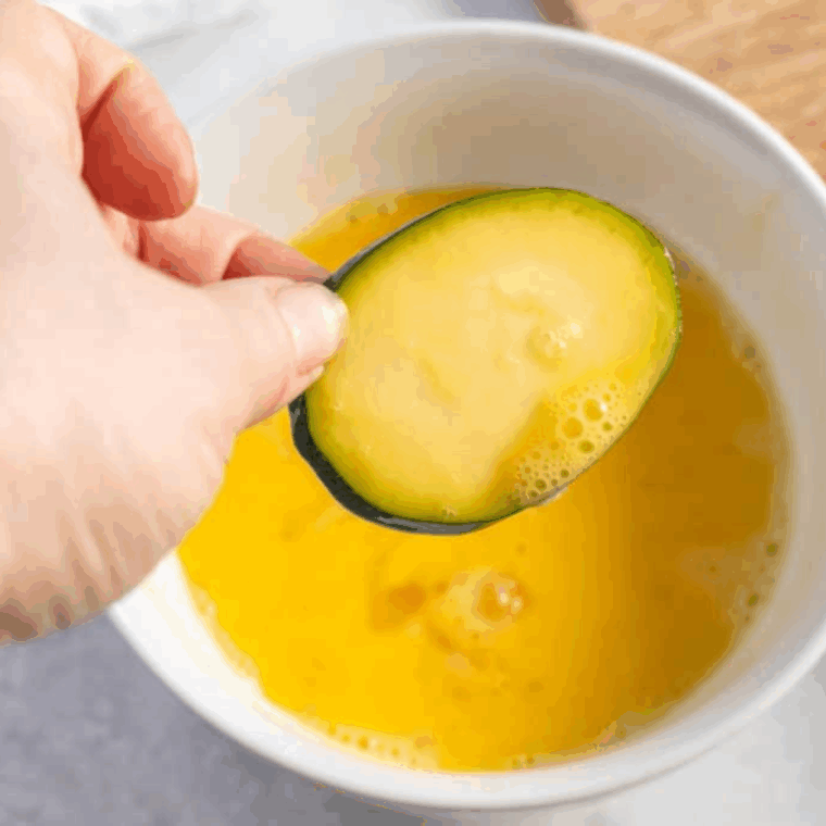 Dipping the zucchini slices into the beaten egg.