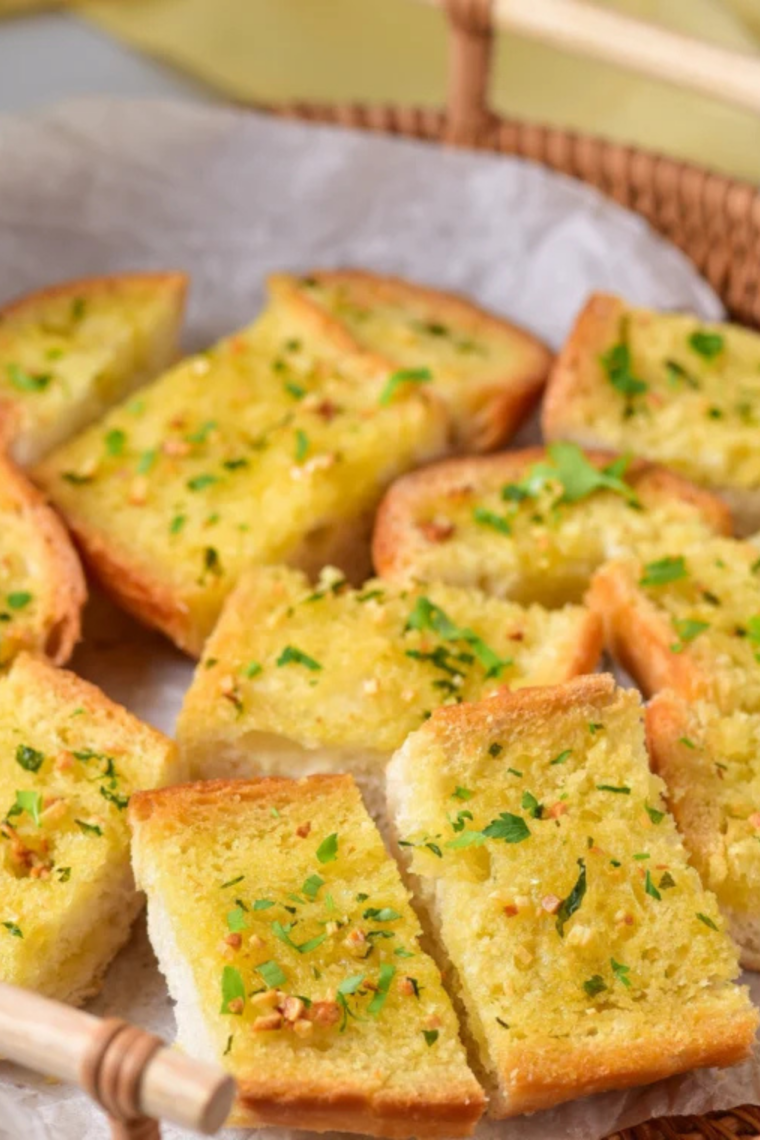 Freshly cooked garlic bread halves in air fryer, showing crispy texture and melted herb butter topping.