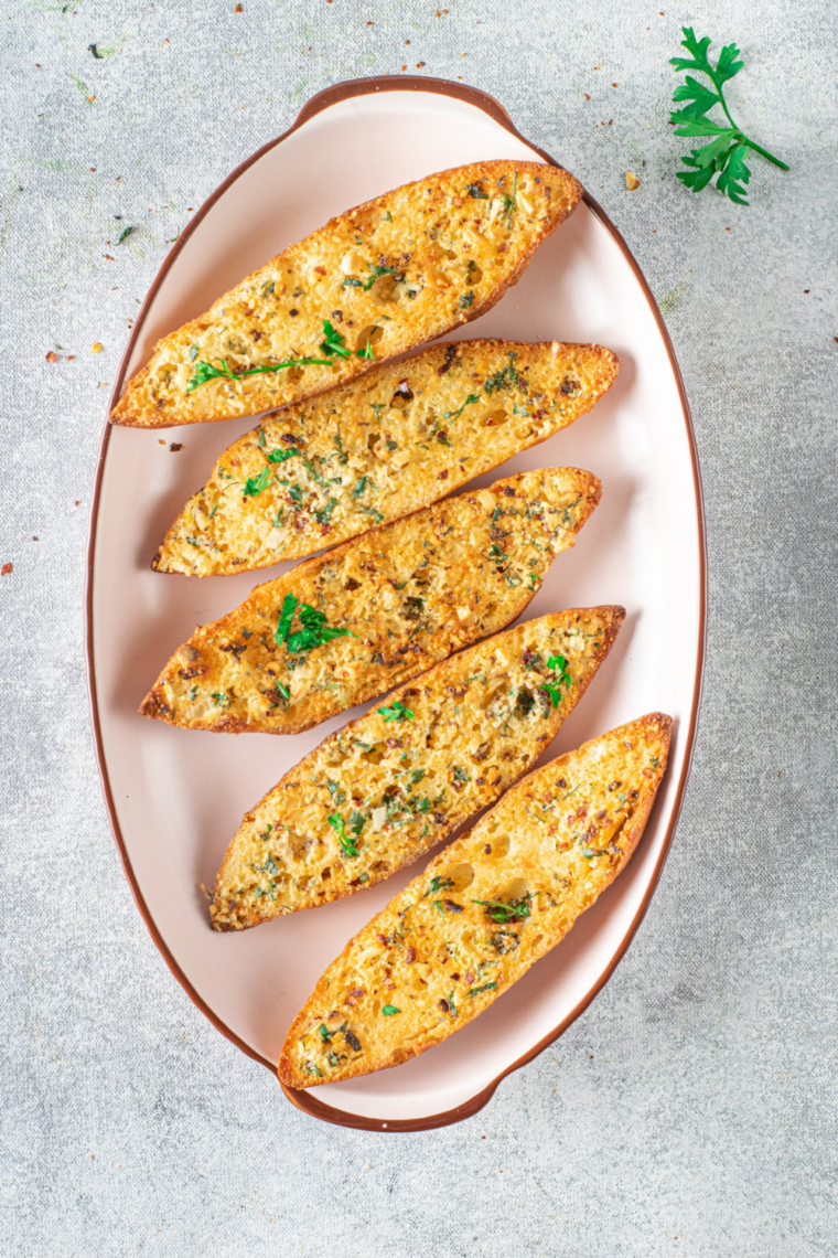 Close-up of air fryer garlic bread slices with toasted edges and visible herbs like parsley and basil.