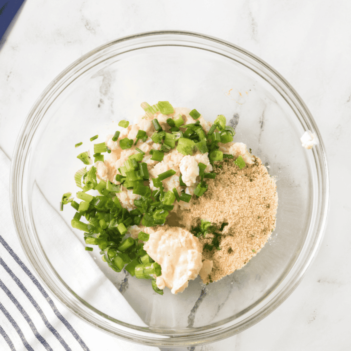 Mixing lump crab meat, green onion, mayonnaise, bread crumbs, lemon zest, and lemon juice together in a small bowl for crab cakes