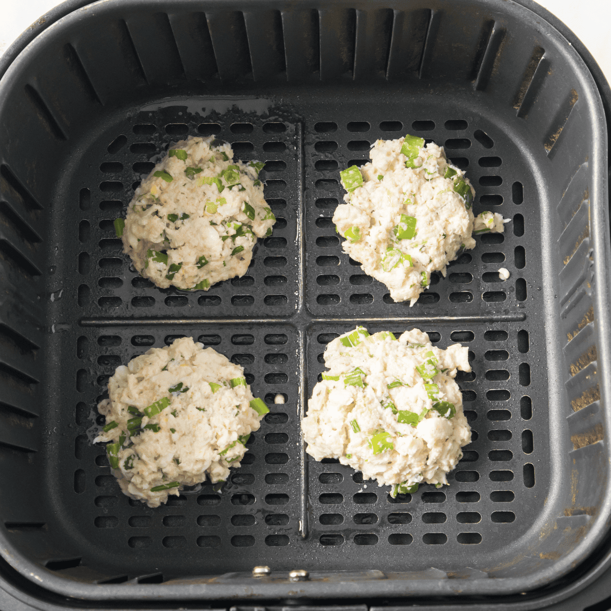 Raw crab cakes in the air fryer basket, ready for air frying.