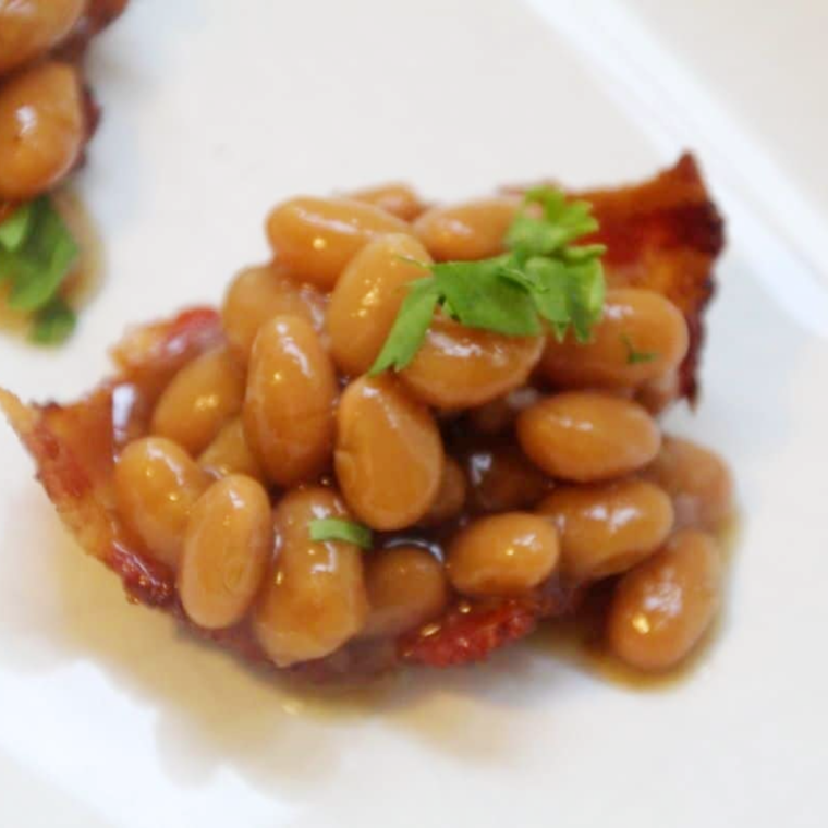 Baked Bean Bacon Cups on a plate, filled with baked beans and sprinkle of parsley on top