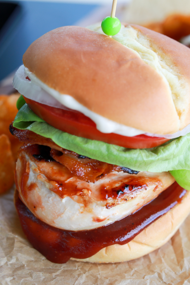 Freshly made BBQ chicken burgers on a Blackstone griddle ready for serving with crispy bacon and cheese.
