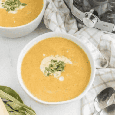 Bowl of creamy copycat Costco butternut squash soup topped with toasted pumpkin seeds and a swirl of coconut milk