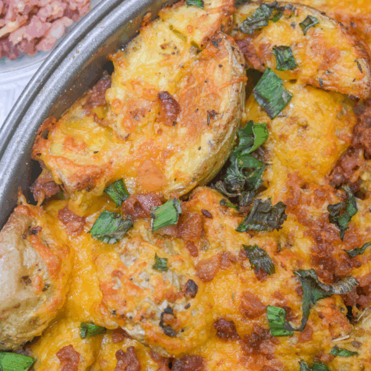 Crispy air fryer loaded baby potatoes topped with melted cheese, bacon bits, and chopped green onions, served in a white dish.