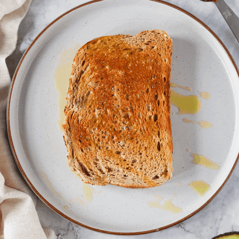 Piece of toast on a plate, drizzled with olive oil.