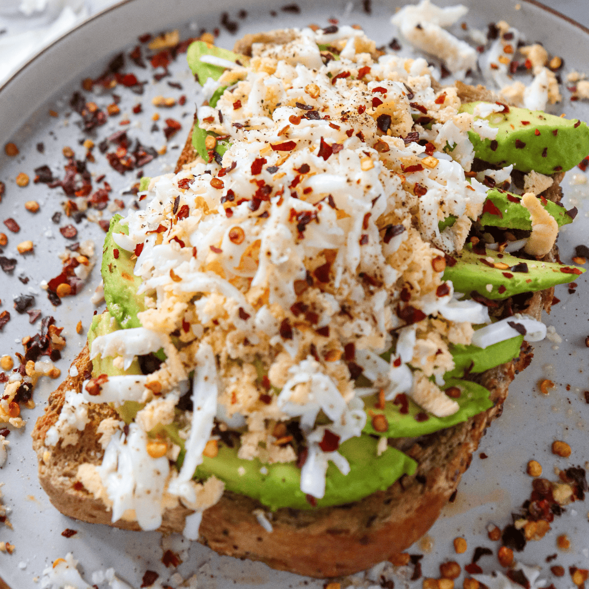 A plate of Air Fryer Grated Egg & Avocado Toast, topped with creamy avocado and a grated egg for added texture.