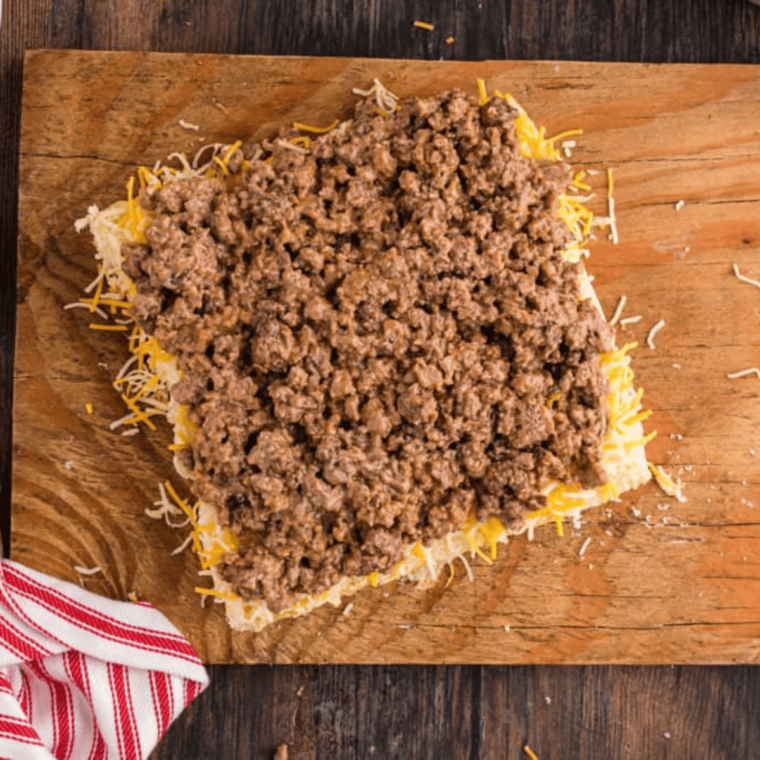 overhead: cooked ground beef from air fryer over shredded cheese on a cutting board