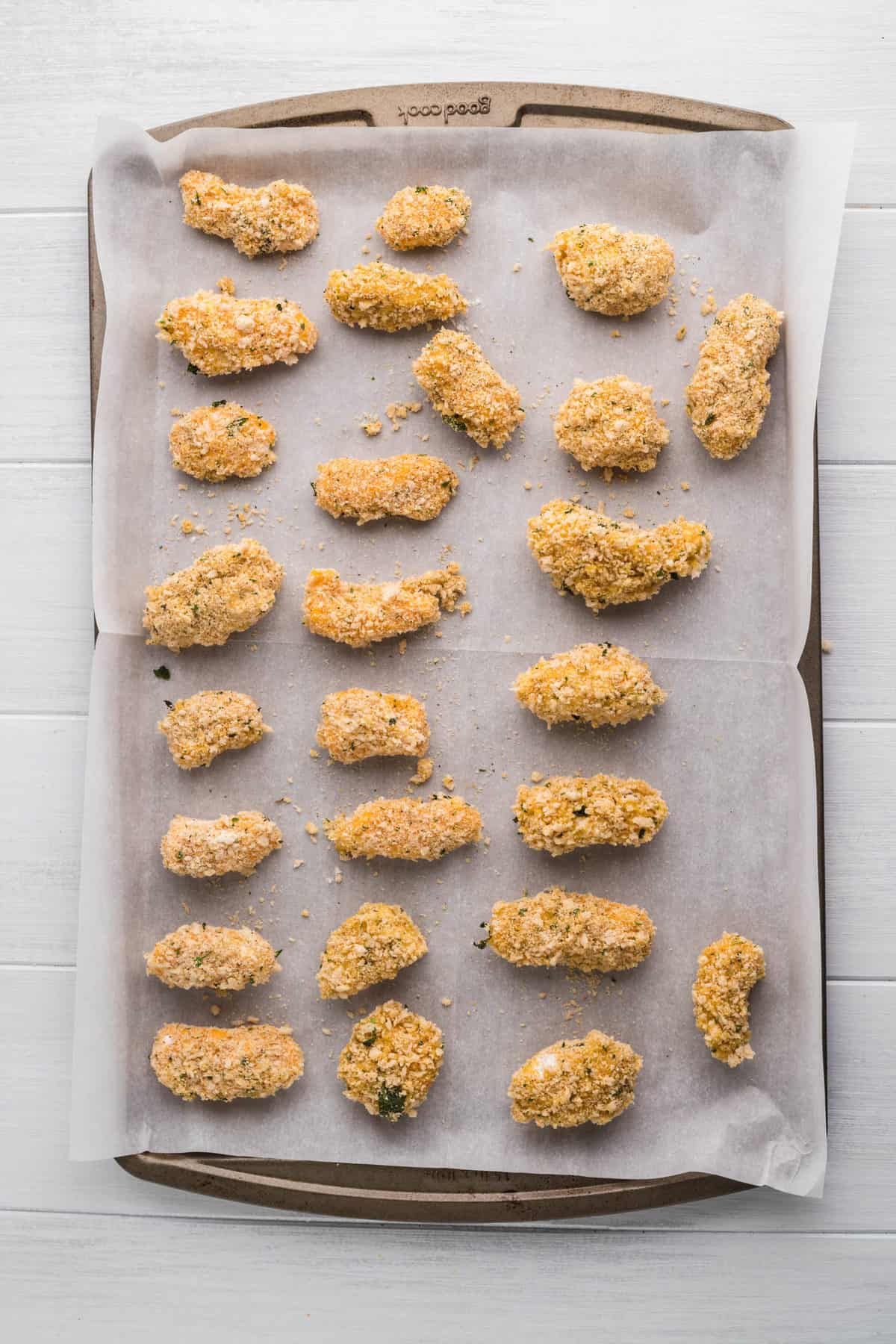 Top view of a baking sheet lined with parchment paper with breaded but uncooked Air Fryer Cheese Curds on it. 