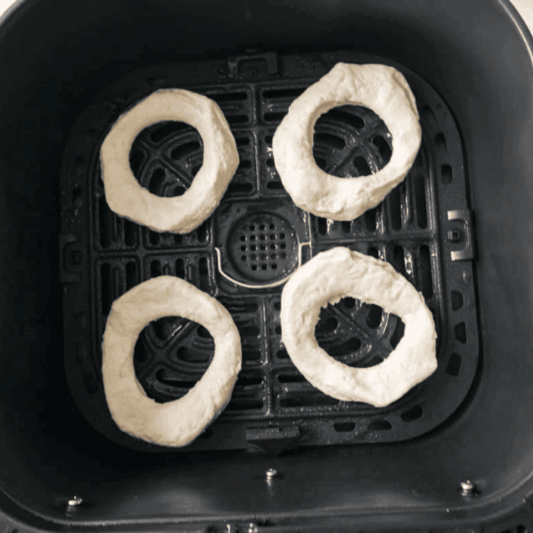 Cutting donut holes from biscuits and spraying air fryer basket to prevent sticking.