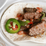 Air fryer steak fajitas with charred peppers and onions piled on a warm flour tortilla