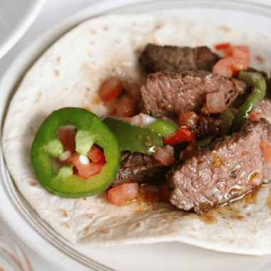Air fryer steak fajitas with charred peppers and onions piled on a warm flour tortilla