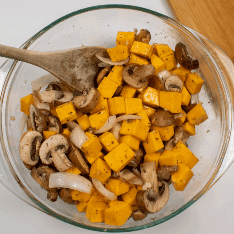 Butternut squash, onion, and mushrooms being tossed in melted butter and herbs.