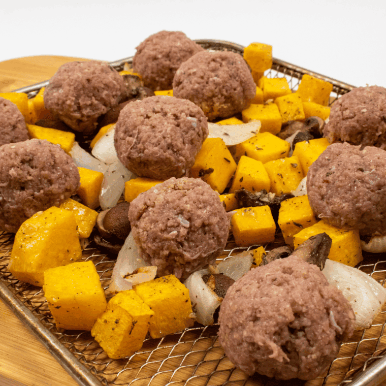 Raw, 1.5-inch turkey sausage meatballs being placed over partially cooked squash.
