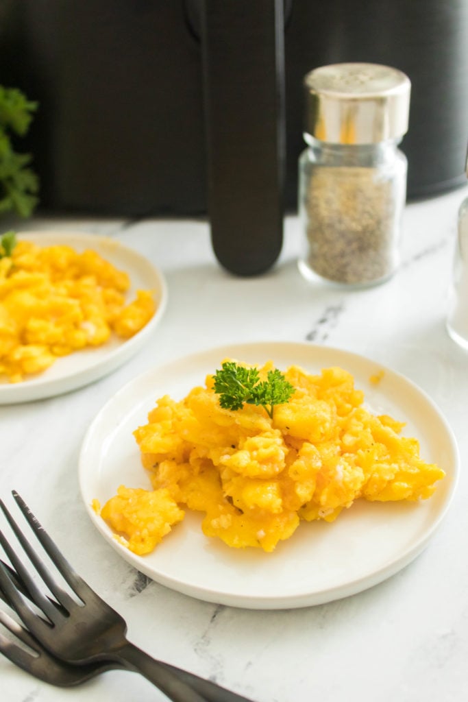 closeup: plate of air fried scrambled eggs next to air fryer, pepper shaker, and forks