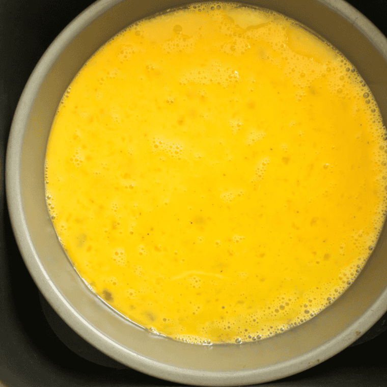 overhead process shot: beaten eggs added to the pan in the air fryer basket