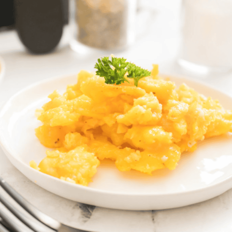 closeup: scrambled eggs made in air fryer on a white plate with fresh parsley on top