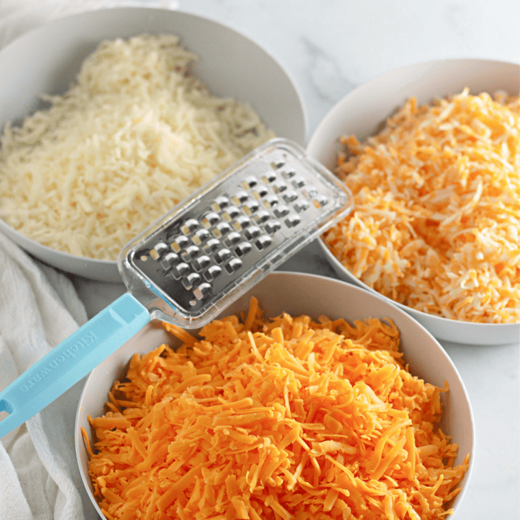Shredded cheddar, Pecorino Romano, and Parmigiano-Reggiano prepped in bowls for copycat Costco mac and cheese