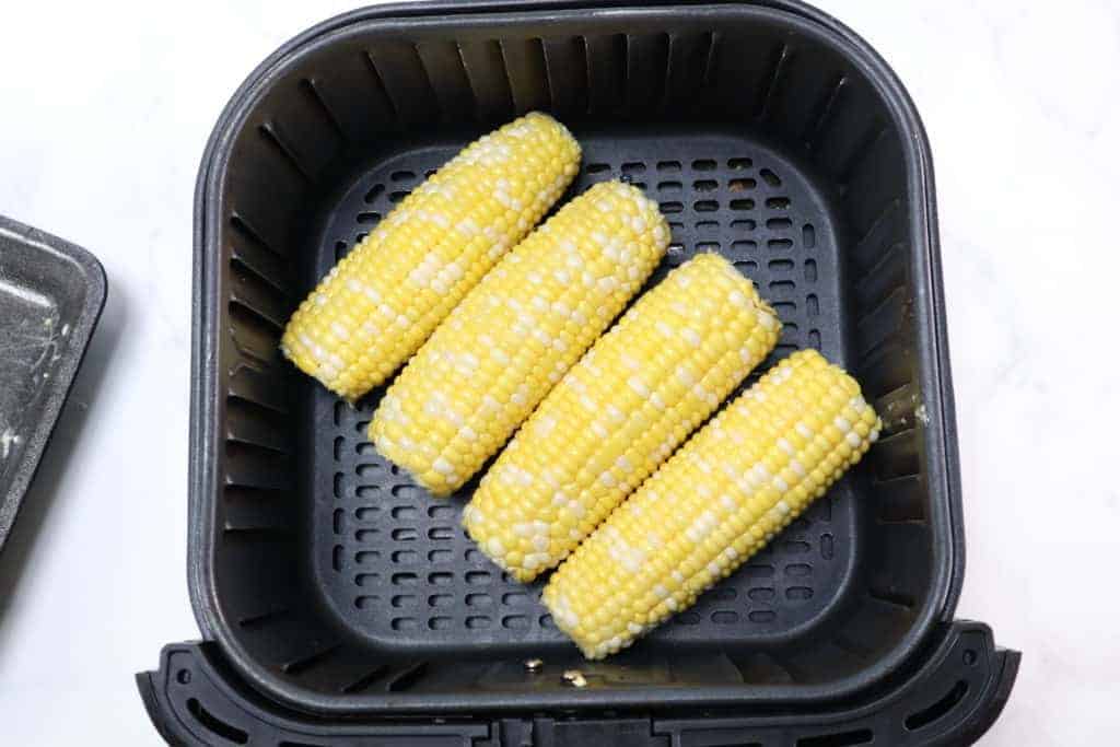 air fryer basket with four pieces of elote corn