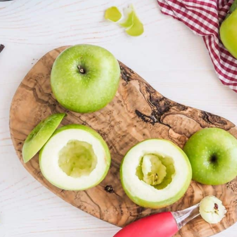 Cutting the tops off apples and using a spoon to remove the seeds and core before filling with pie filling.