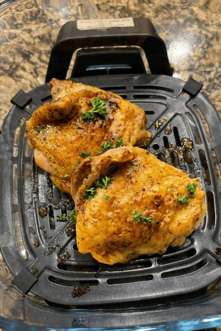 Golden-brown air fryer chicken thighs cooked in a Ninja Crispi, garnished with fresh herbs on a plate.