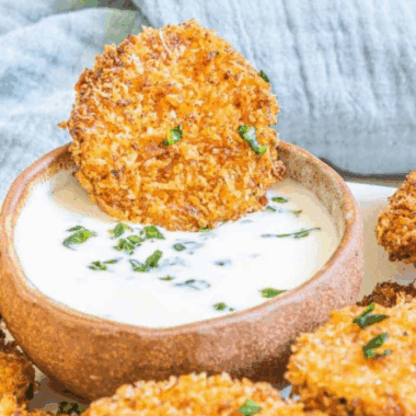 Golden air-fried zucchini crisps coated in parmesan cheese, served on a plate for a crunchy snack or appetizer.