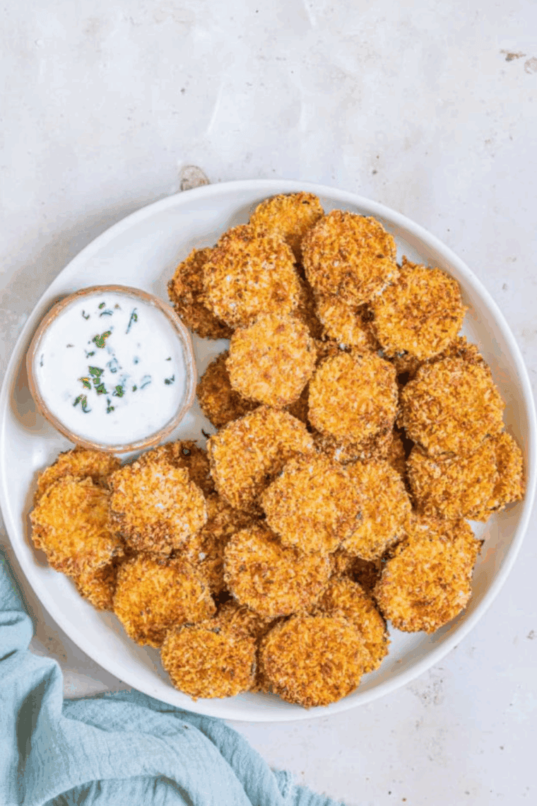 Crispy zucchini slices coated in golden parmesan crust, served hot from the air fryer on a white plate.