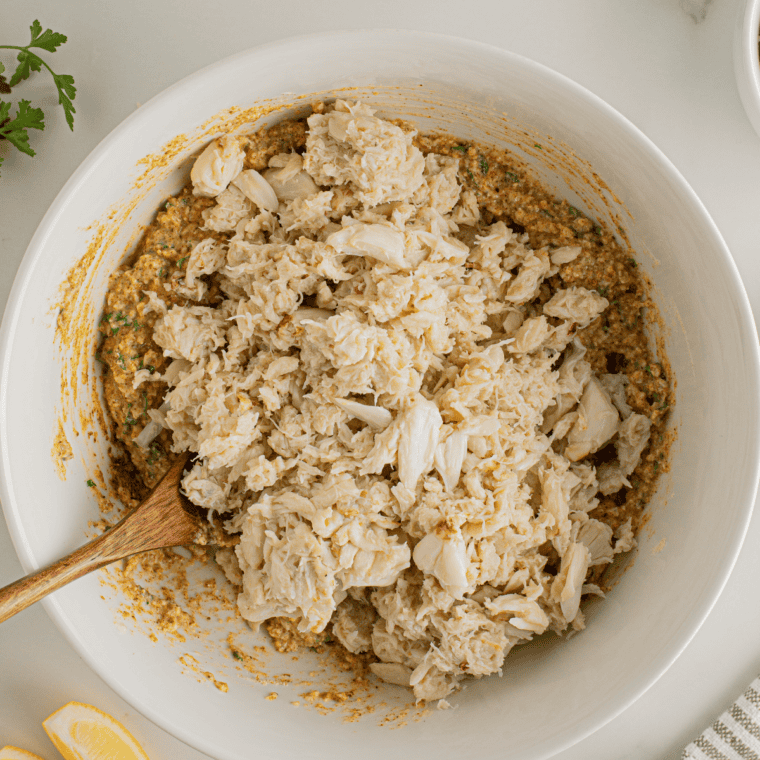 Crab cake mixture ingredients whisked together in a glass bowl including mayo, egg, Dijon, lemon juice, and Old Bay before adding crab.