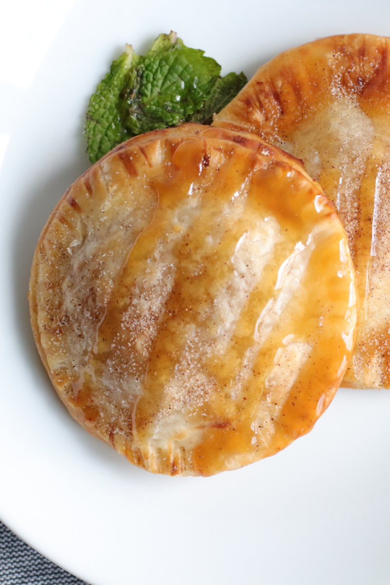 Caramel apple hand pies on a white plate with vanilla ice cream and caramel drizzle