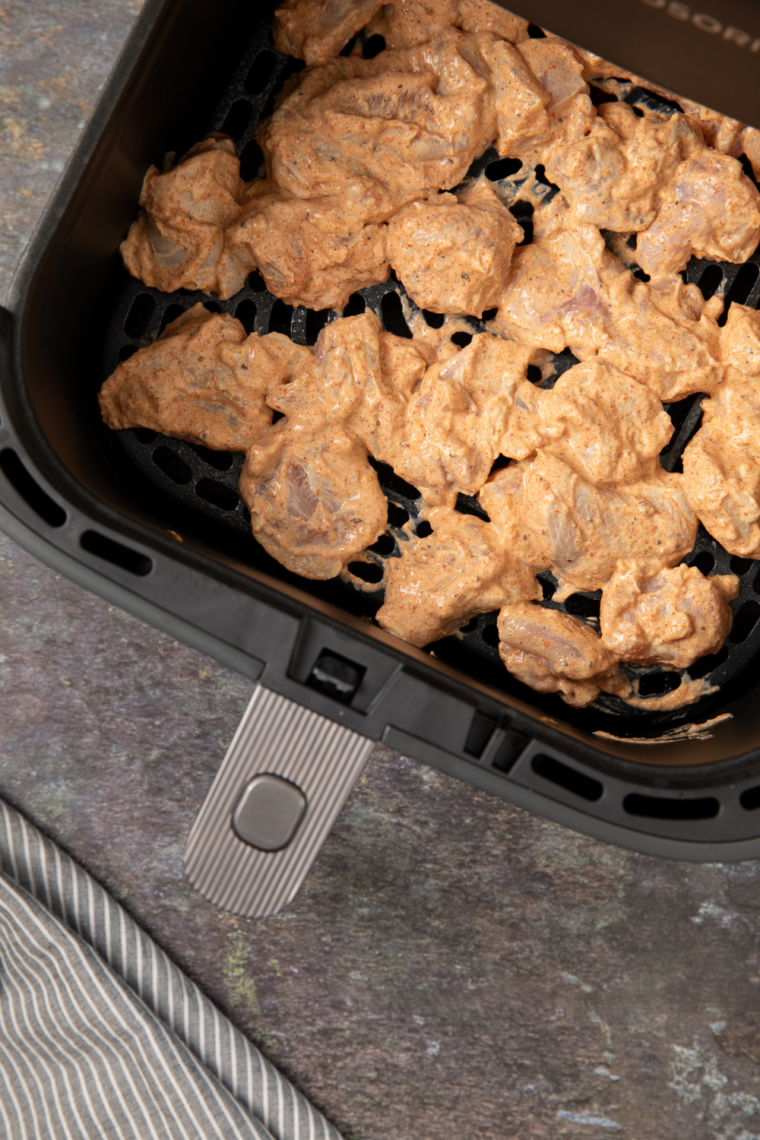 Chicken pieces arranged in the air fryer basket, cooking to golden and slightly charred perfection.