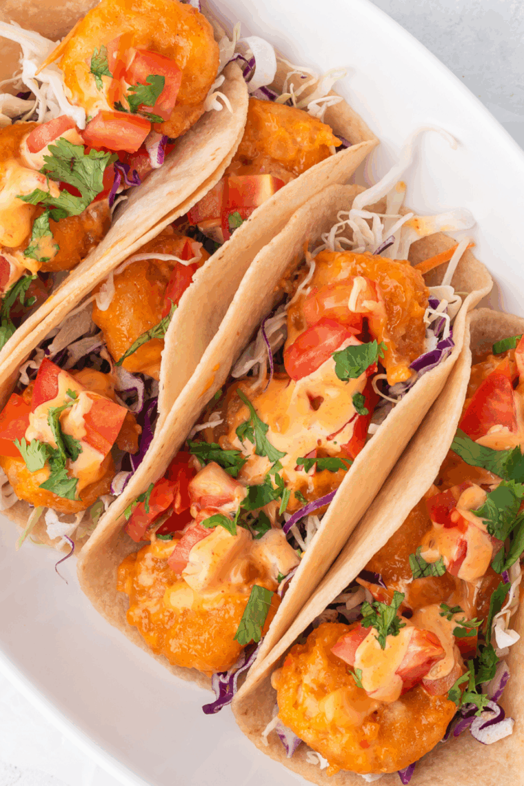 Air fryer shrimp tacos with frozen shrimp, topped with lettuce, tomatoes, avocado, and sauce