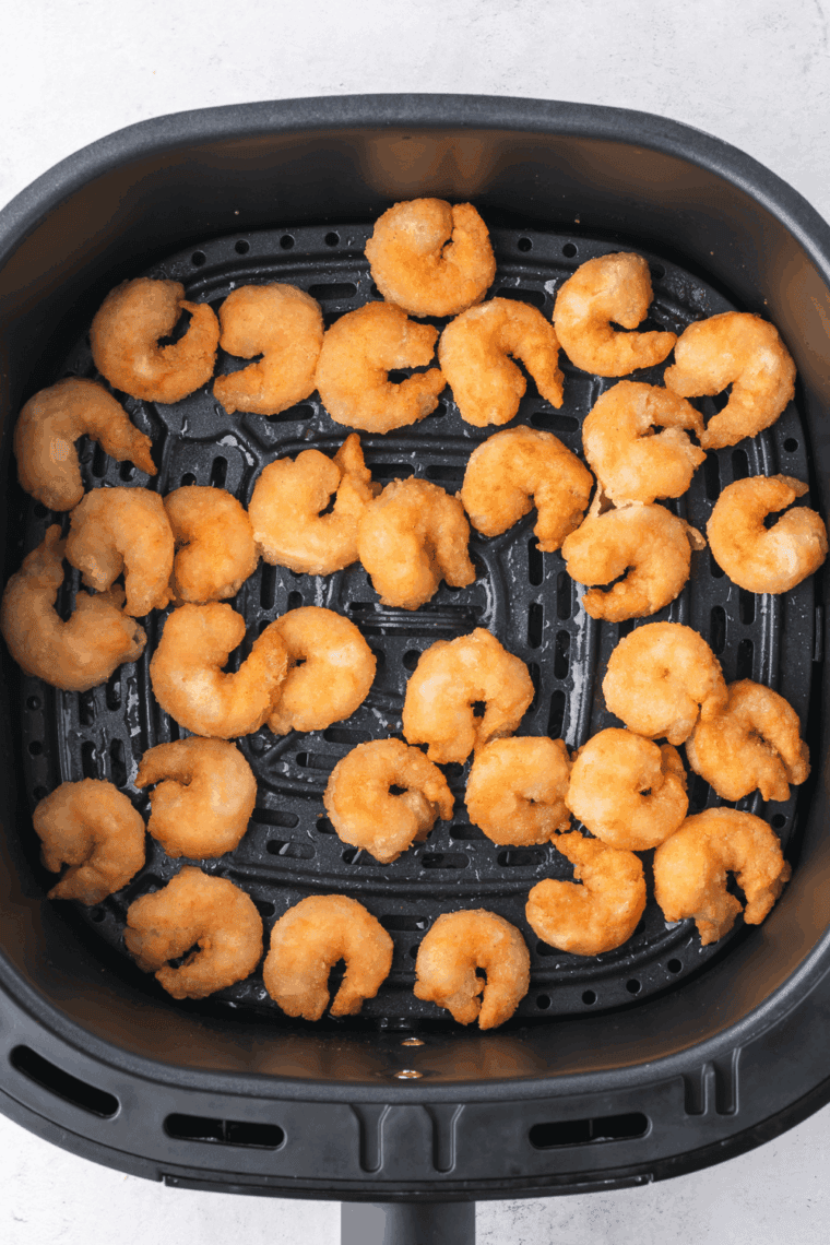 Shrimp cooking in a single layer in air fryer basket, turning halfway