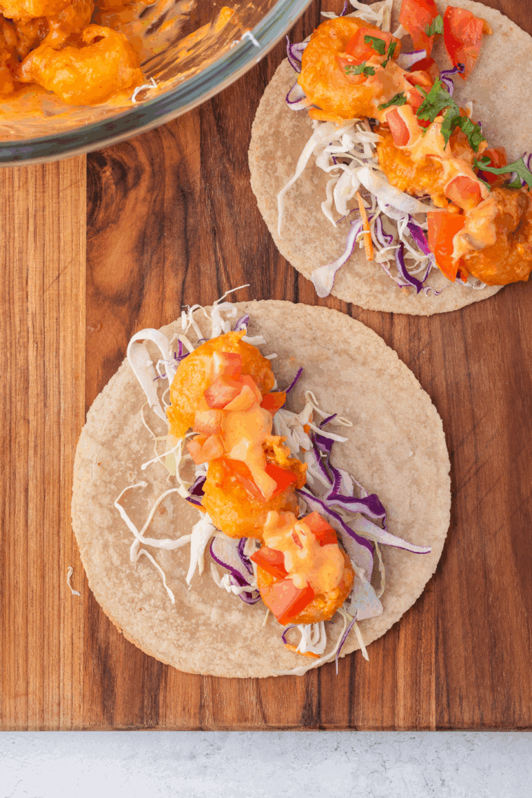 Air-fried shrimp placed in taco shells, topped with lettuce, tomatoes, avocado, cheese, and sauce